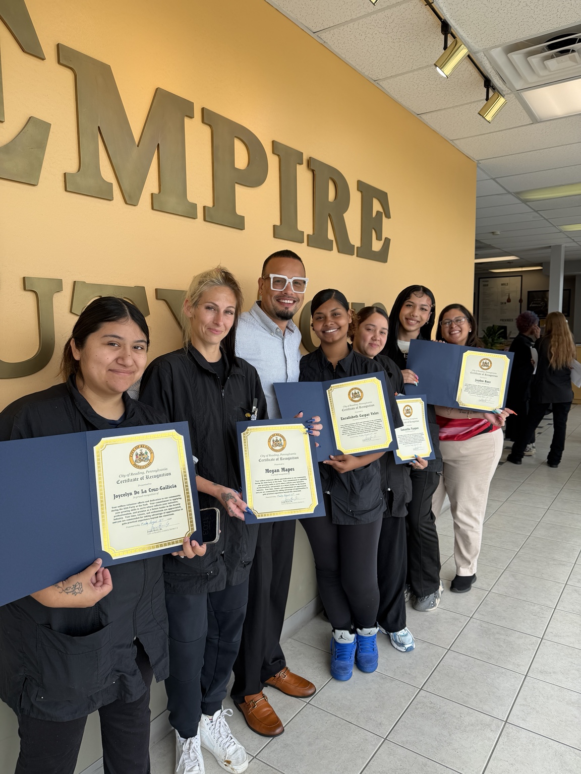 Jaime standing with a group holding certificates of recognition at Empire Beauty School