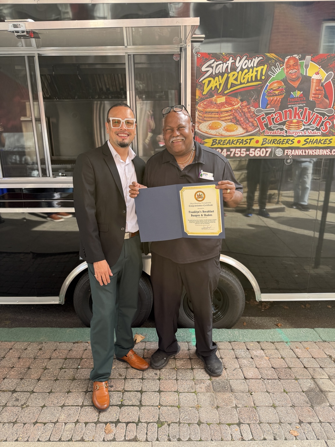 Jaime with a community member holding a certificate for Franklyn’s in front of its food trailer